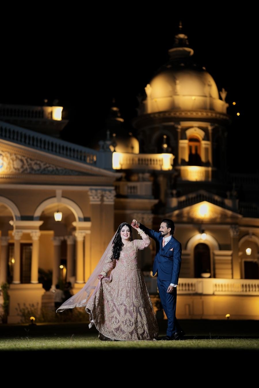 Bride and groom twirl in front of a domed palace at night